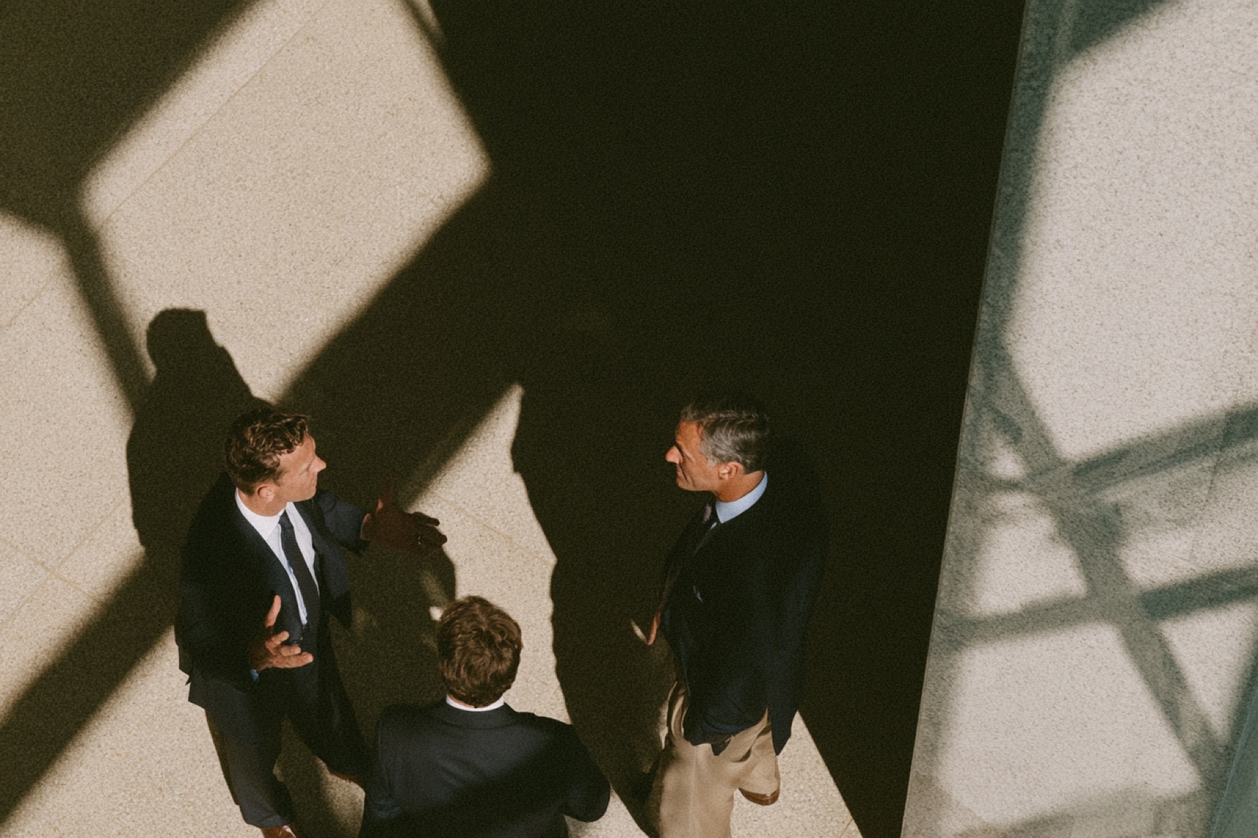 Three people talking in a stone courtyard, seen from above in hard sunlight