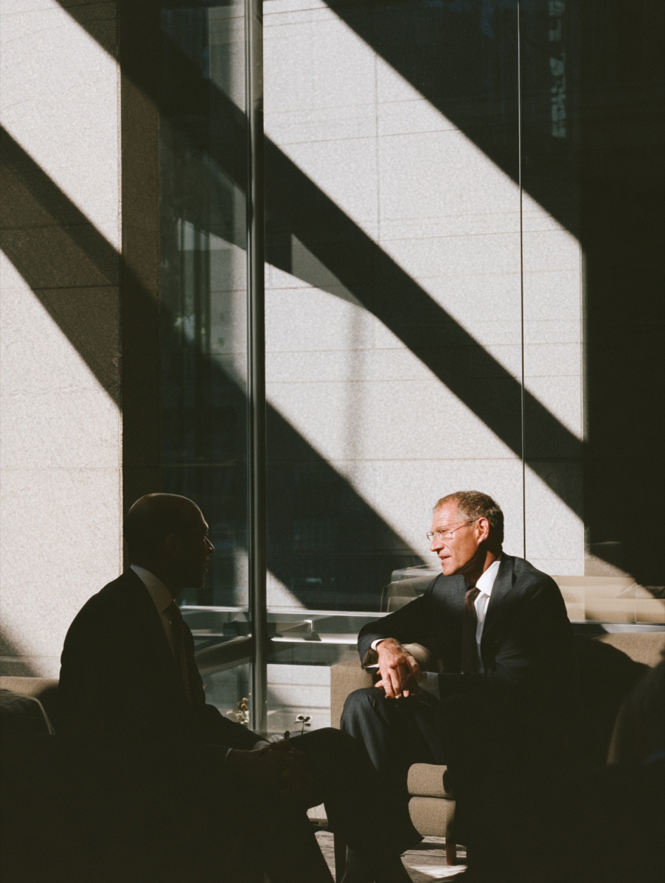 Two people in conversation in an atrium cut by diagonal shadows