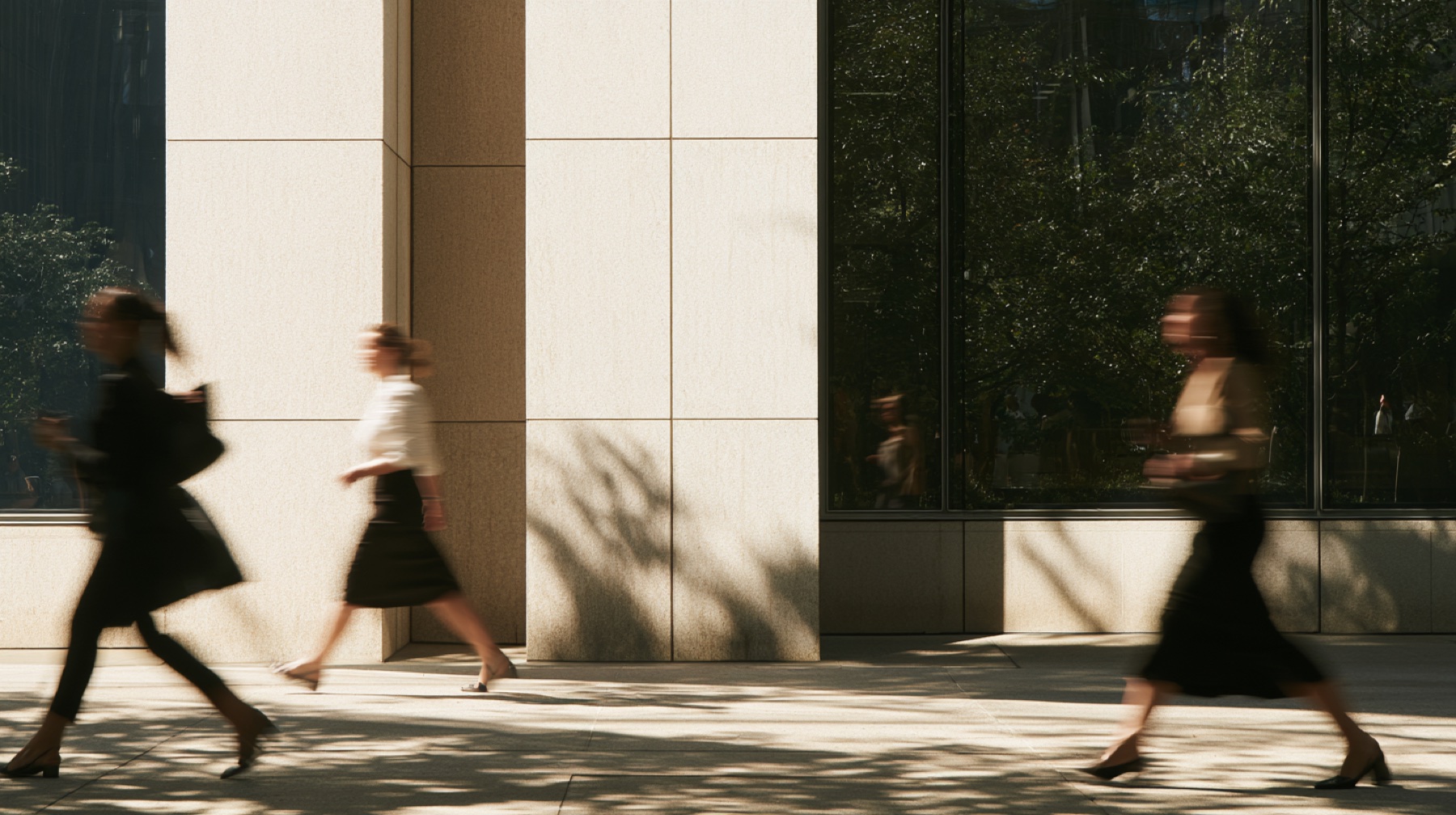 Three people walking past a limestone facade in dappled afternoon light