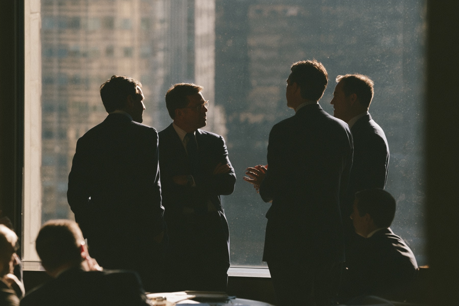 Four people in suits talking against a city skyline window