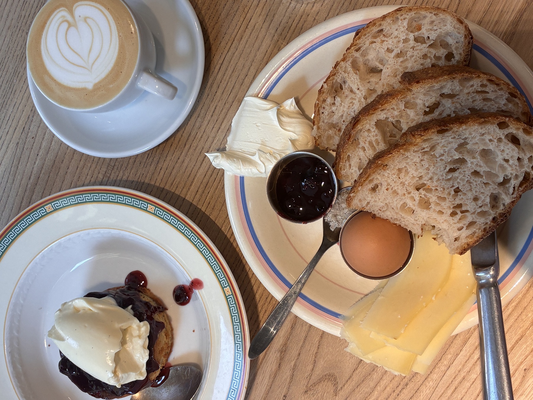 A breakfast plate of bread, egg, cheese and jam beside a cappuccino
