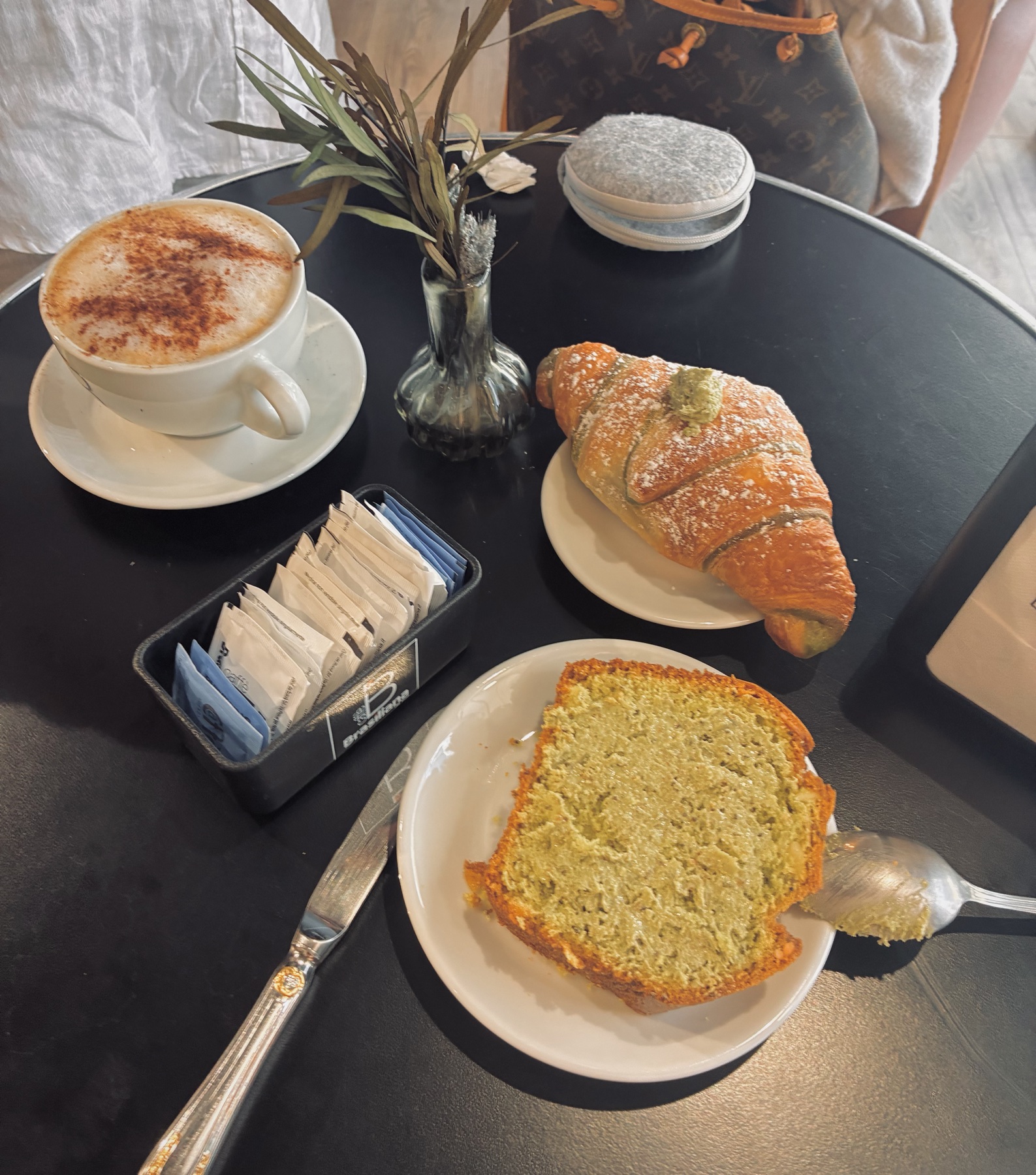 Pistachio croissant, pistachio cake and a cappuccino on a black table