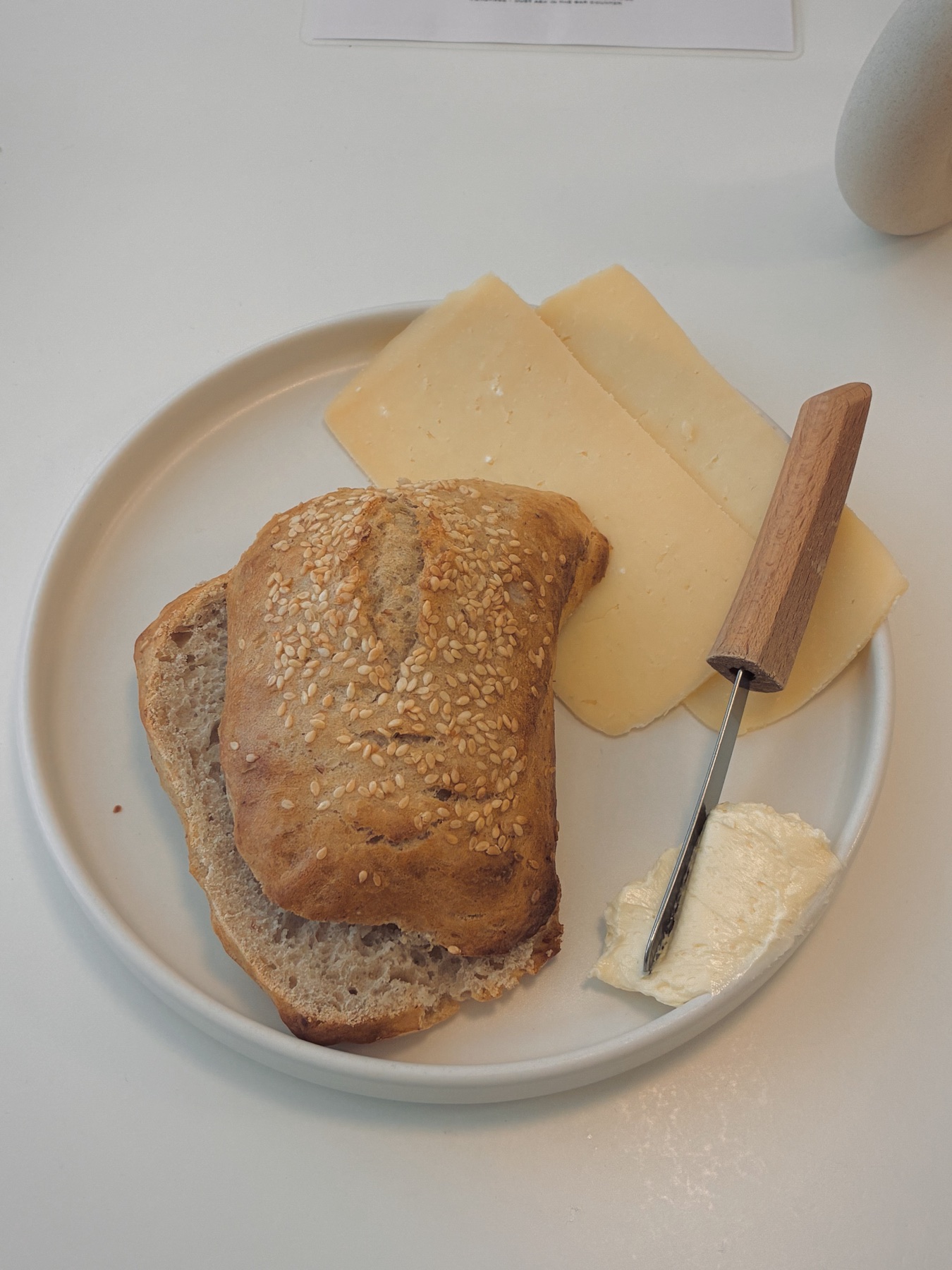 A seeded bun with cheese slices and butter on a white plate